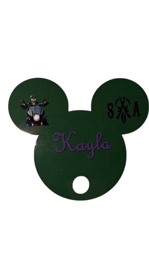 A green mickey mouse shaped tag with the name kayla and an image of a bear.